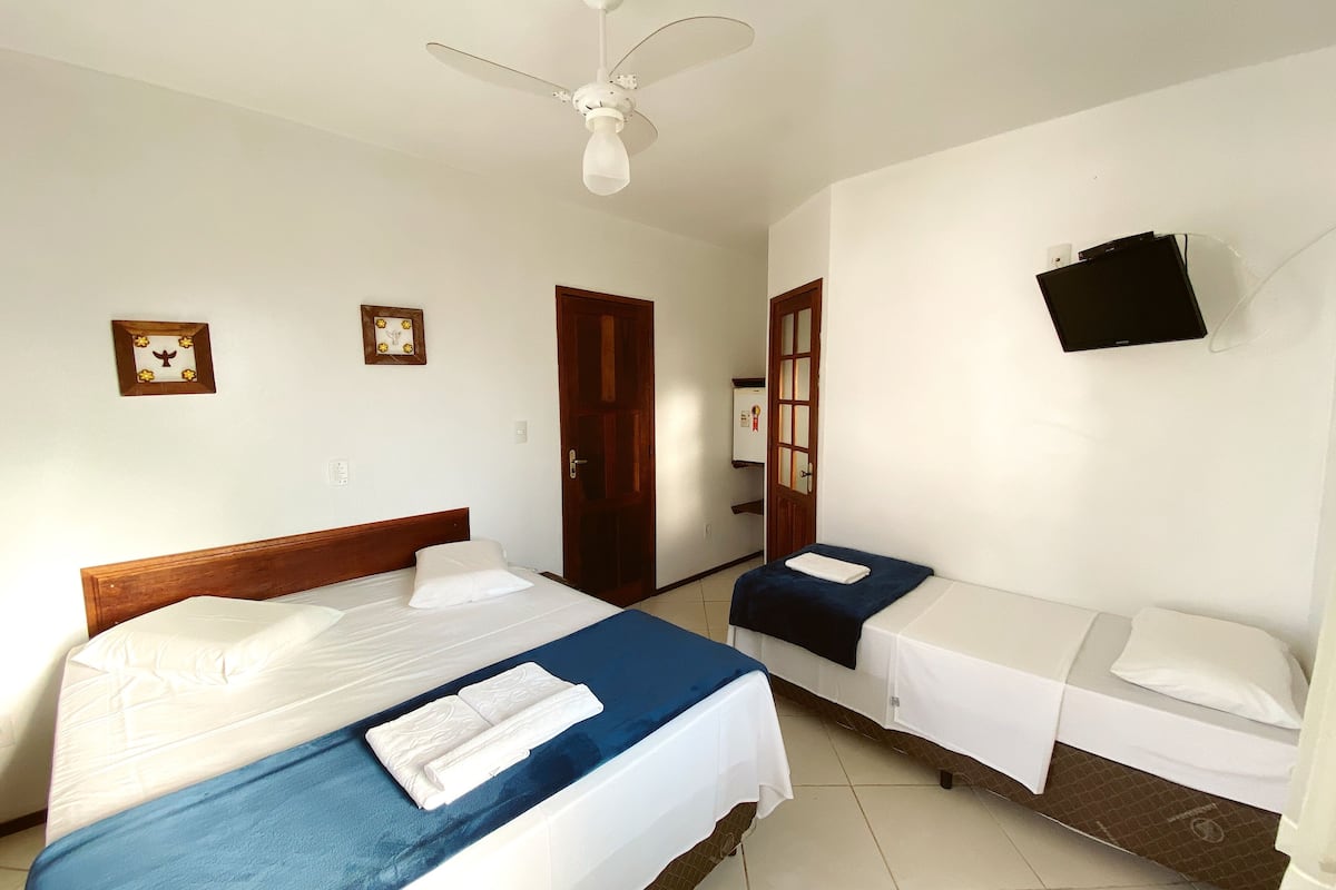 Habitación de hotel con dos camas, ventilador de techo, televisor montado en la pared y puerta con marco de madera.