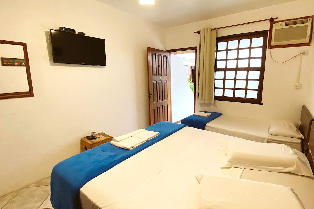 Una habitación con dos camas, un televisor en la pared y un ventanal con cortinas.