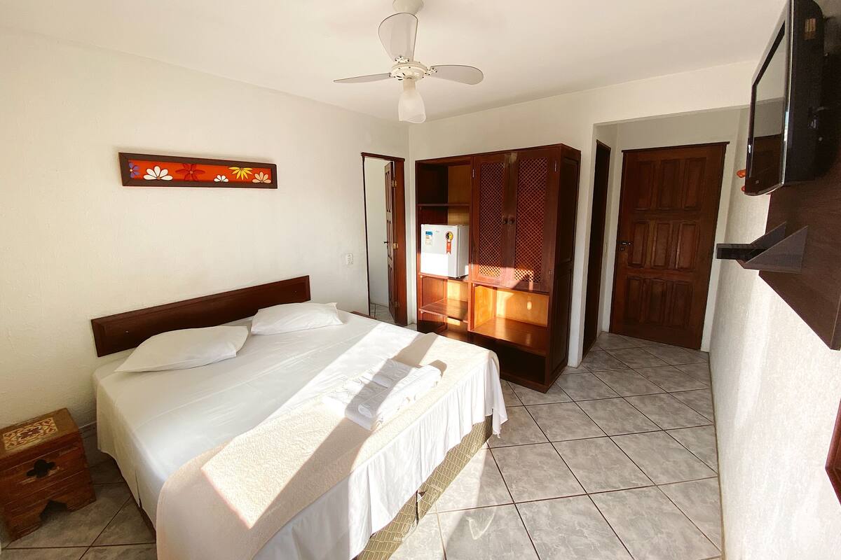 Habitación de hotel con cama, ventilador de techo, televisión y armario.
