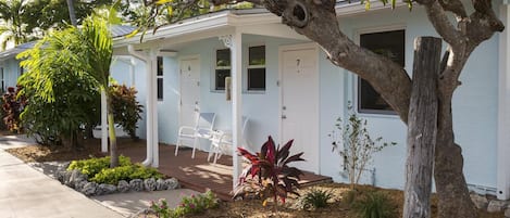 A single-story house with a covered porch, a small garden with various plants, and a number 7 door.