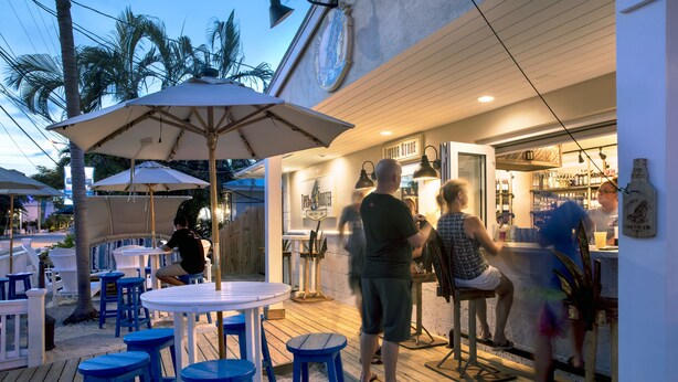 An outdoor bar area with wooden tables and blue stools, a bar counter, and a sign that reads "Liqour Store".