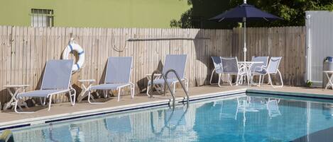 Une piscine entourée d’une clôture en bois, avec des chaises longues et une table à proximité.
