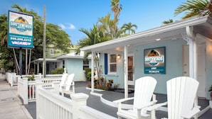 A motel with a porch, white chairs, and a signboard.