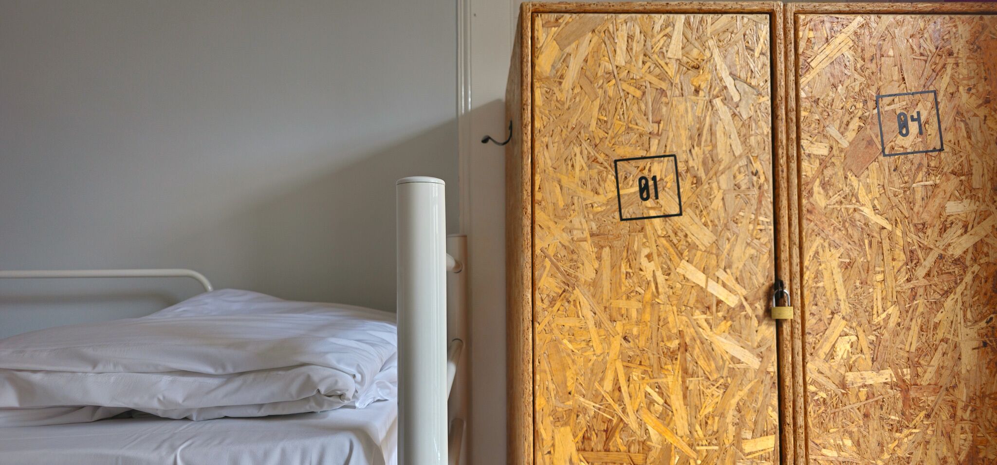 A single bed with white bedding in a room with a wooden door marked with numbers 01 and 04.