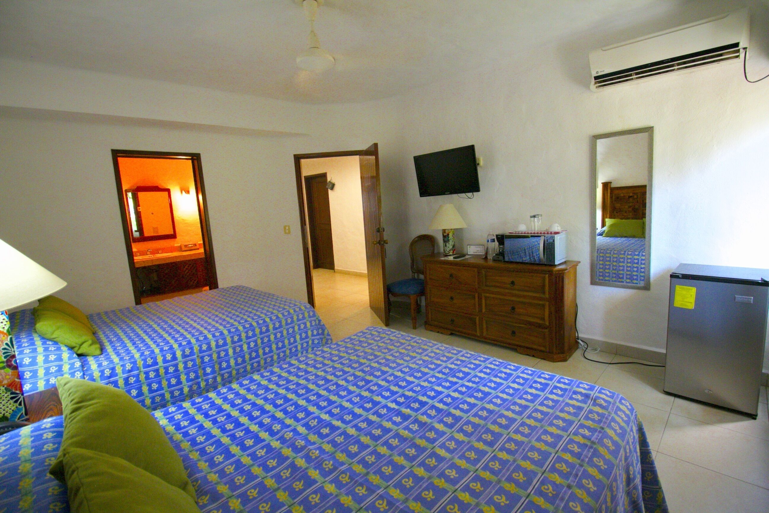 A hotel room with two beds, a television, a dresser, and a refrigerator.