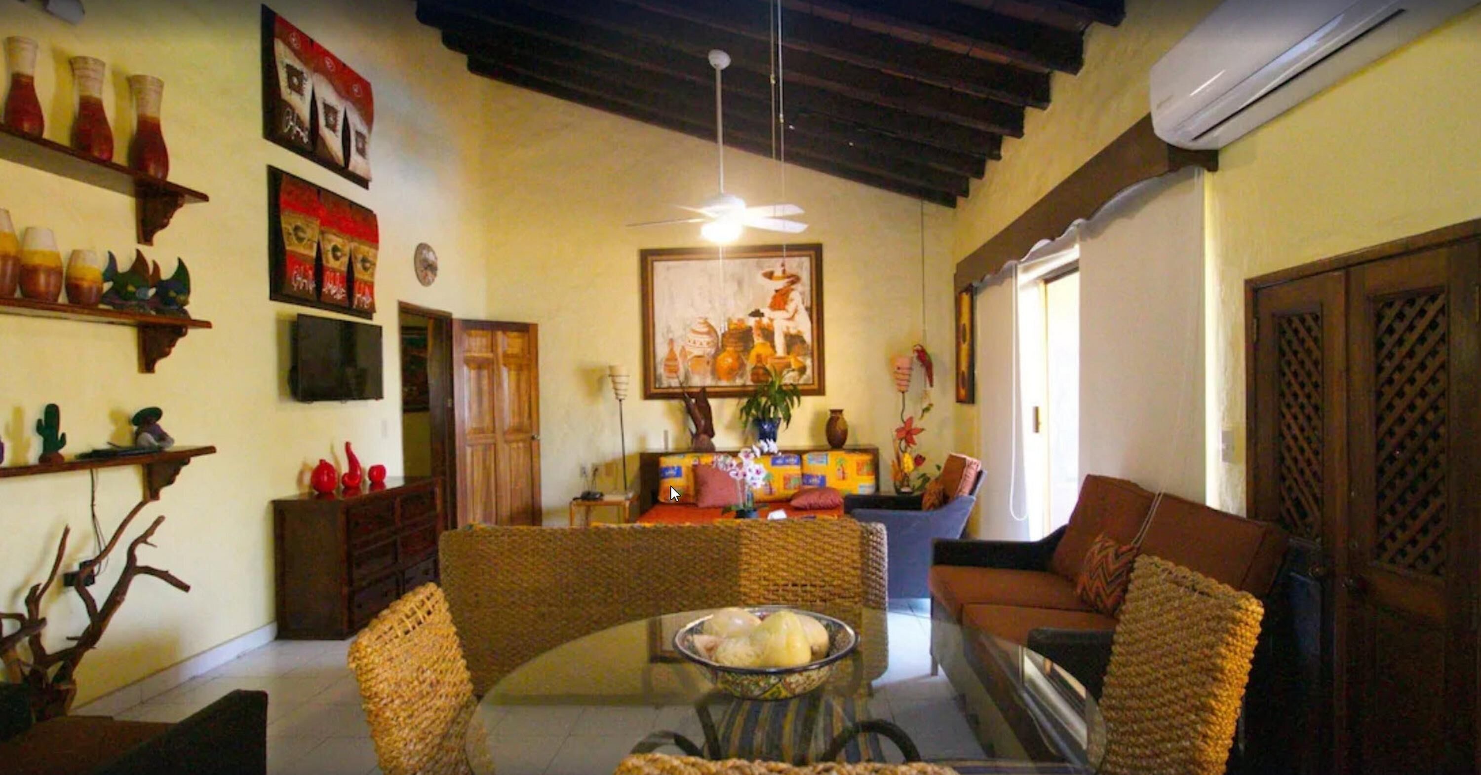 A cozy living room with wicker furniture, a glass coffee table, and a ceiling fan.