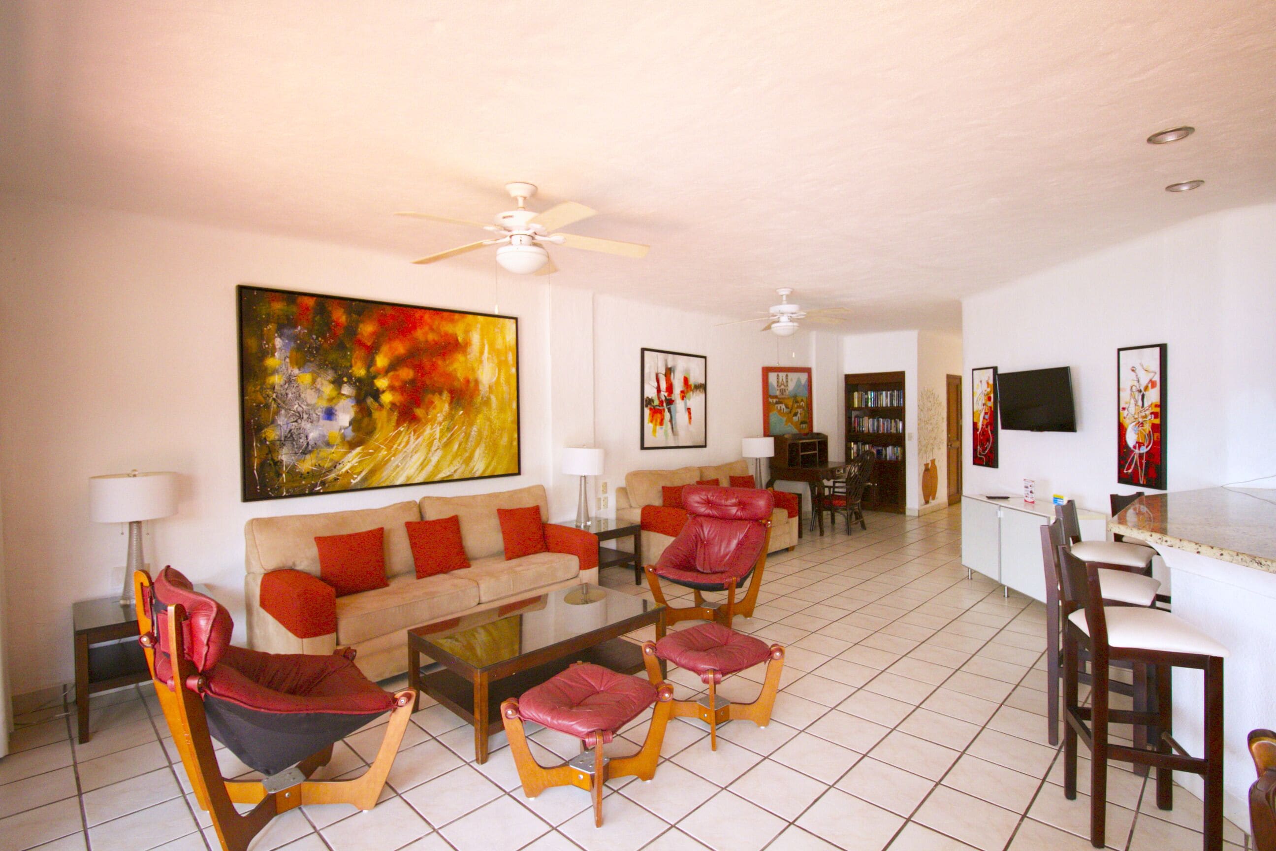A spacious living room with a sofa, red chairs, a coffee table, and a TV.