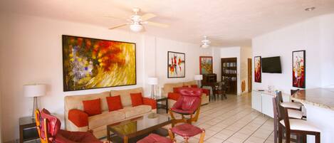 A spacious living room with a sofa, red chairs, a coffee table, and a TV.