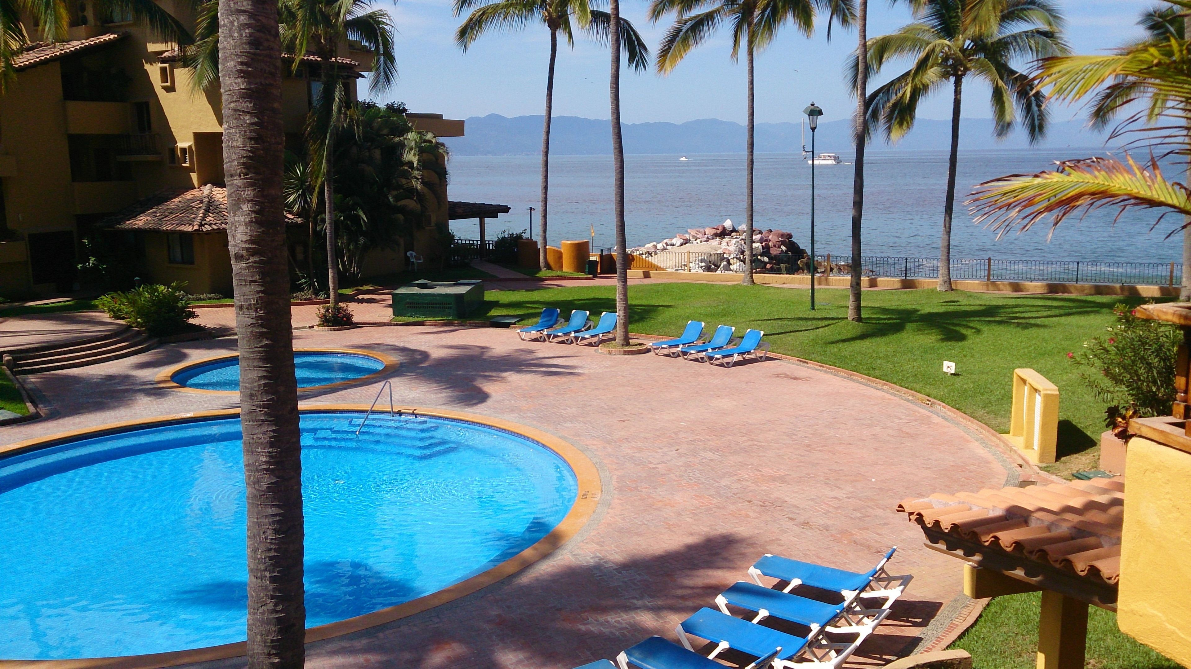 Un área de piscina en un resort, con varias piscinas, sillas de descanso y palmeras.