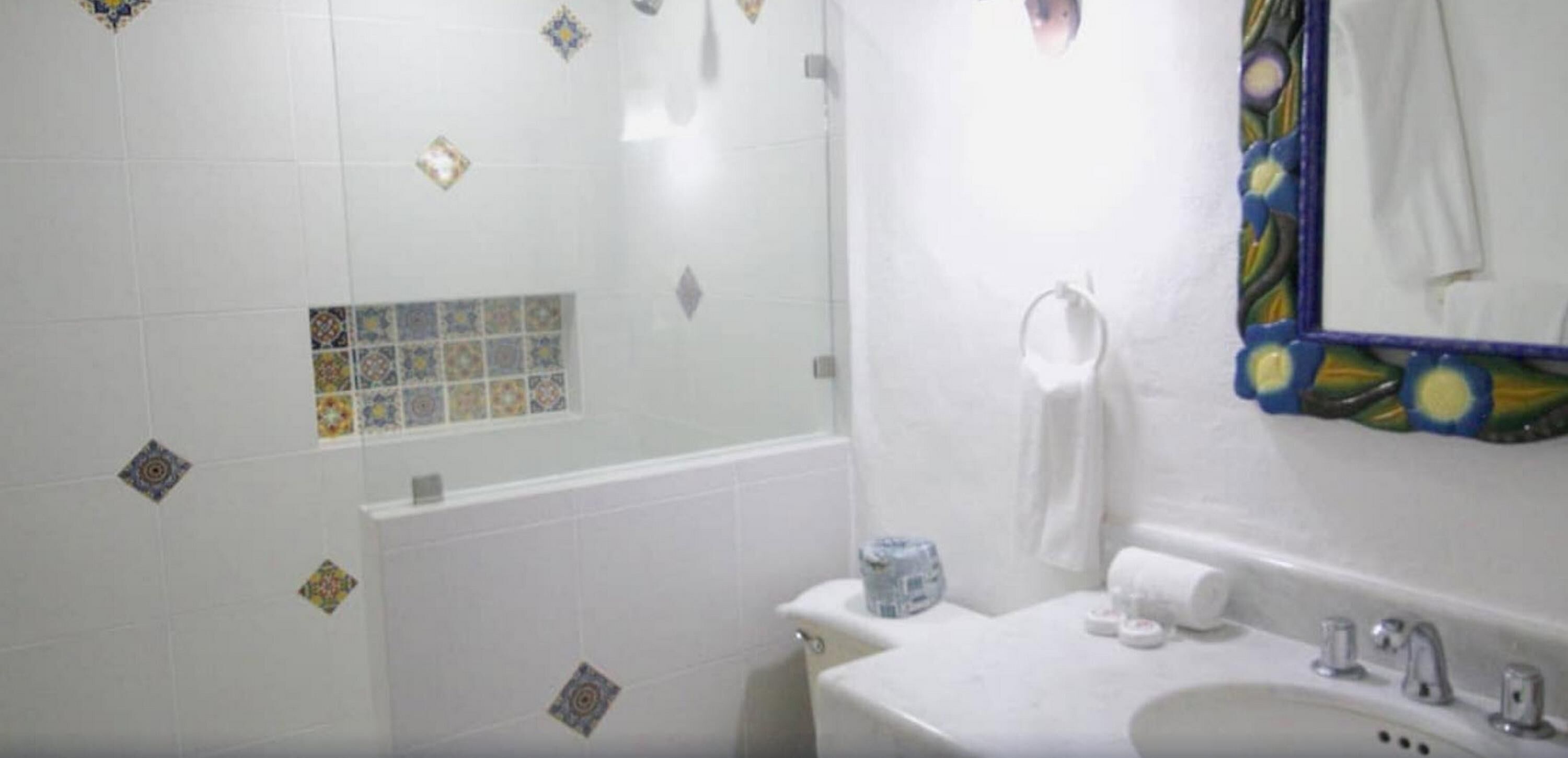 A bathroom with a white sink, a mirror with a decorative frame, and a shower area with patterned tiles.