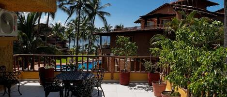 Un patio con piscina, mobiliario exterior, plantas en macetas y un edificio con balcón.