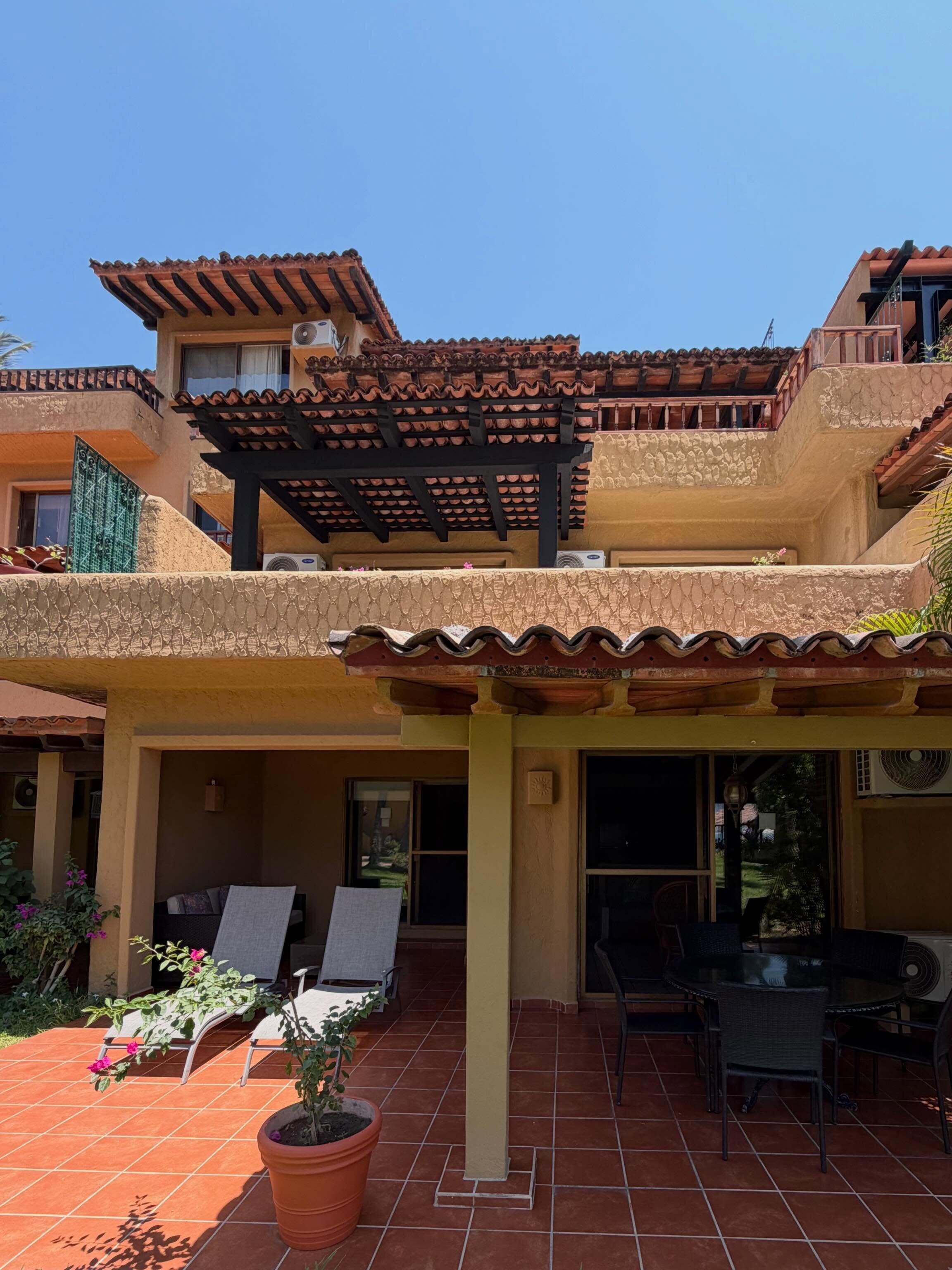 Ein zweigeschossiges Gebäude mit einer Terrasse, die Gartenmöbel und eine Pergola hat.