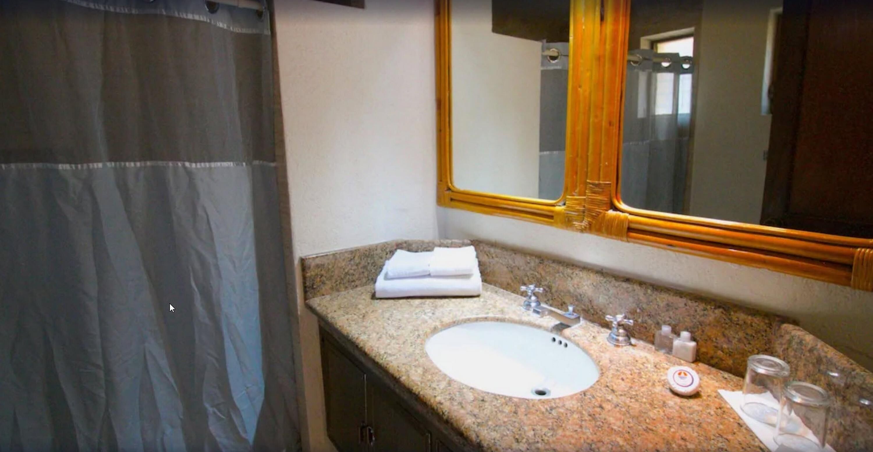 Un baño con lavamanos de encimera de granito, un espejo con marco de madera y una cortina de ducha.