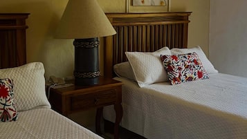 Habitación de hotel con dos camas, una mesita de noche con lámpara, un cuadro enmarcado en la pared y un teléfono sobre la mesa.