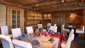 A wooden interior with a dining table set for a meal, white chairs, and a wooden cabinet with glass doors. - Le Clos du Hahnenberg (Urmatt)