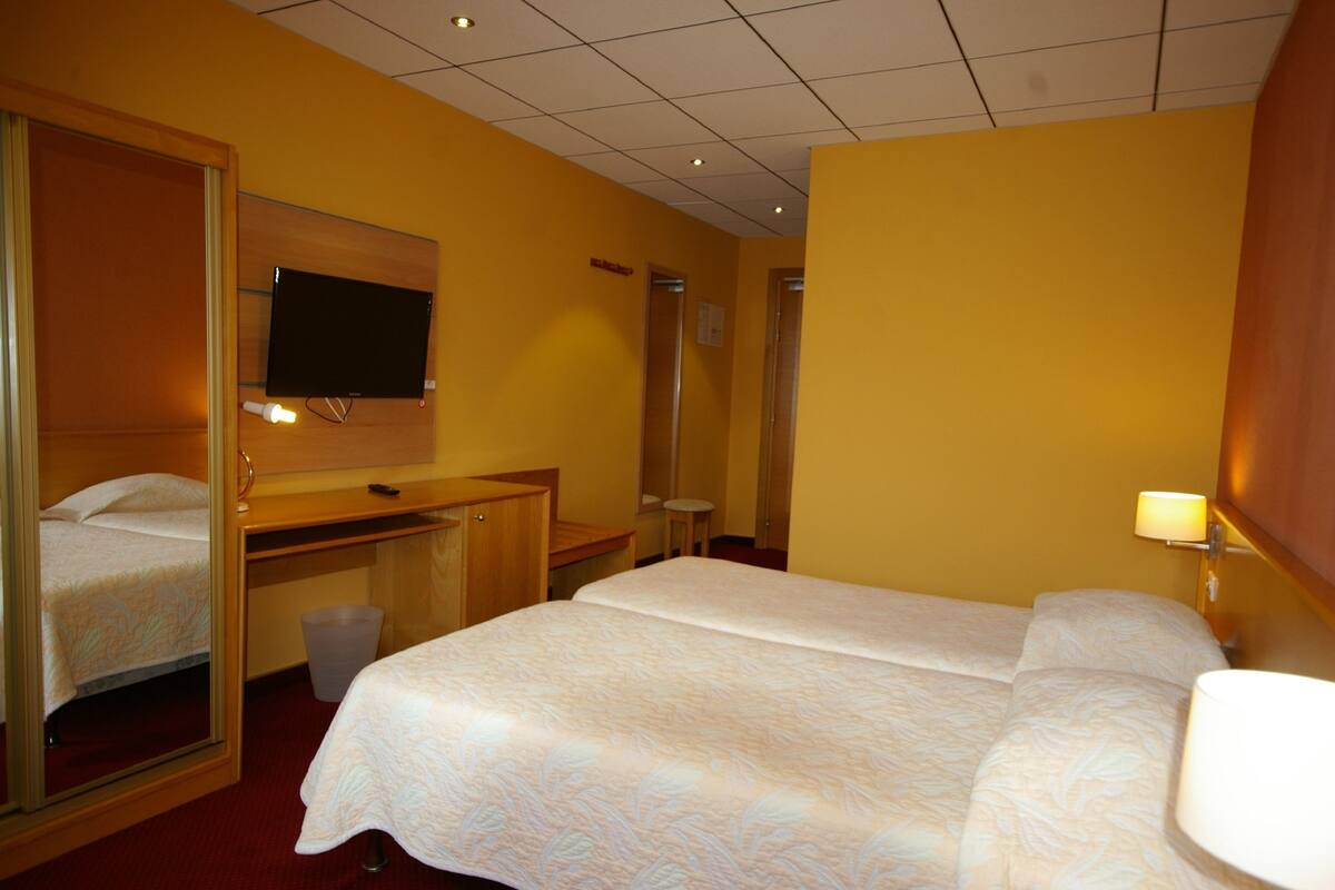 A hotel room with two beds, a desk, a mirror, and a television.