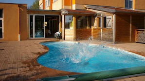 A swimming pool with a wooden deck, adjacent to a building with large windows and a sliding glass door. - Le Clos du Hahnenberg (Urmatt)