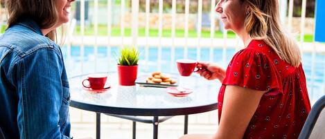 Dos personas sentadas en una mesa redonda con una planta pequeña en maceta, una taza roja y un plato de galletas.