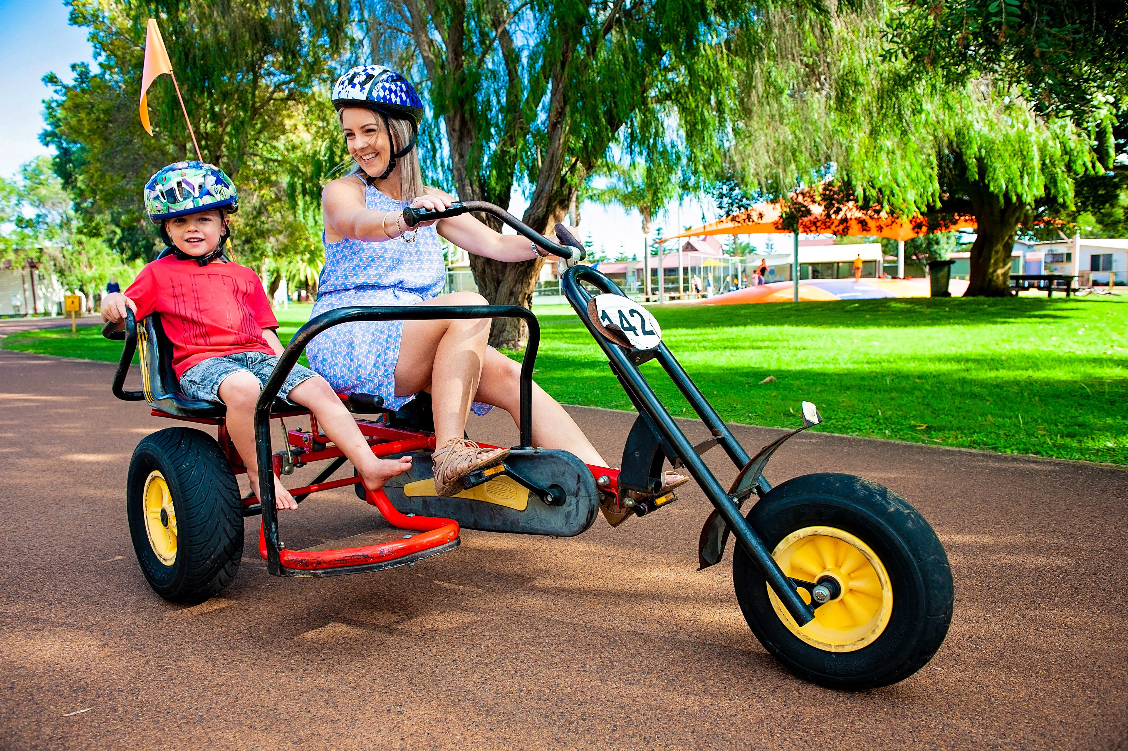 A child and an adult on a tricycle in a park.