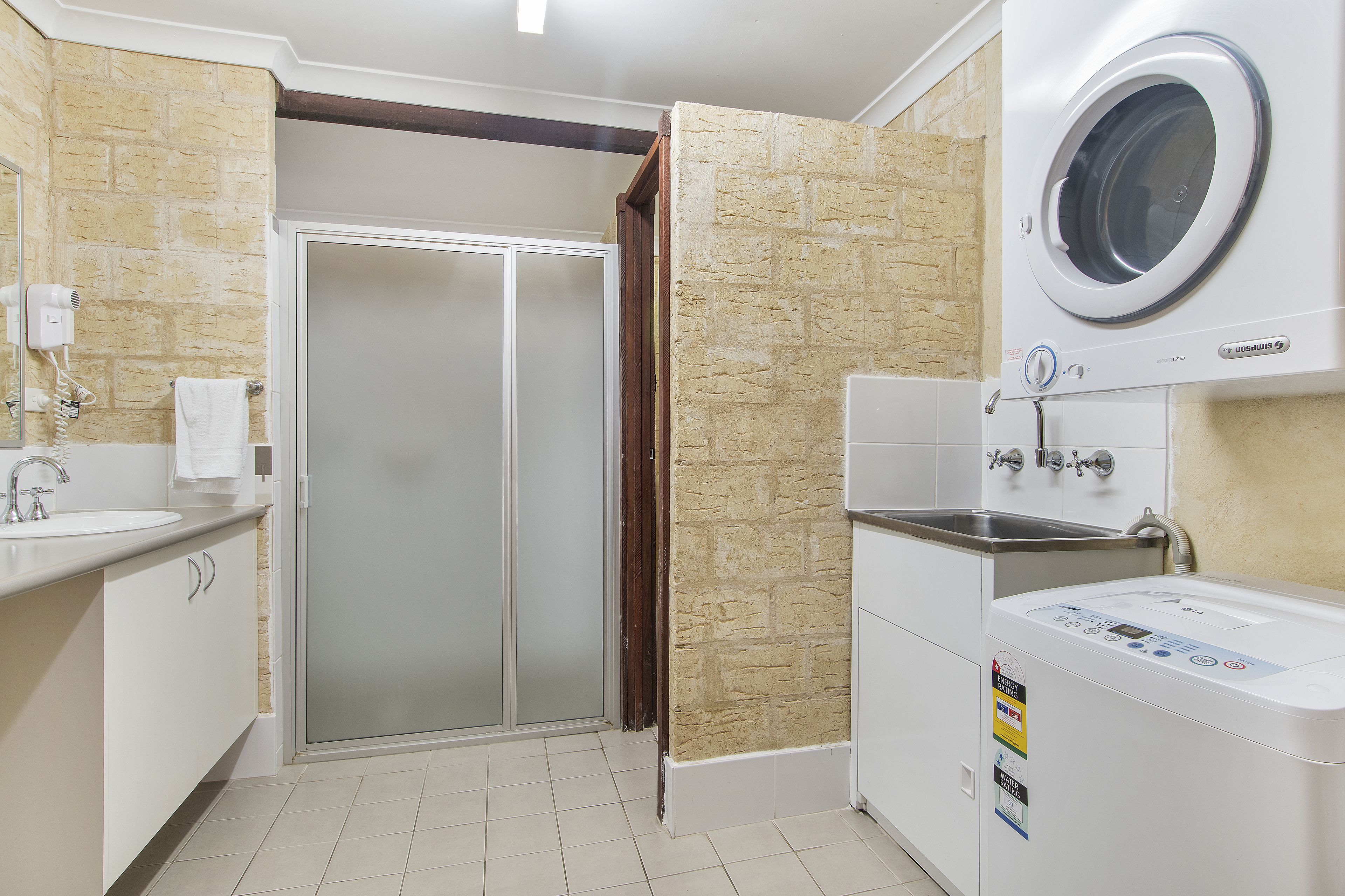 Un baño moderno con puerta de ducha de vidrio, lavadora integrada y un lavamanos con una toalla colgada en la pared.