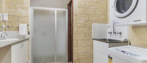 Un baño moderno con puerta de ducha de vidrio, lavadora integrada y un lavamanos con una toalla colgada en la pared.