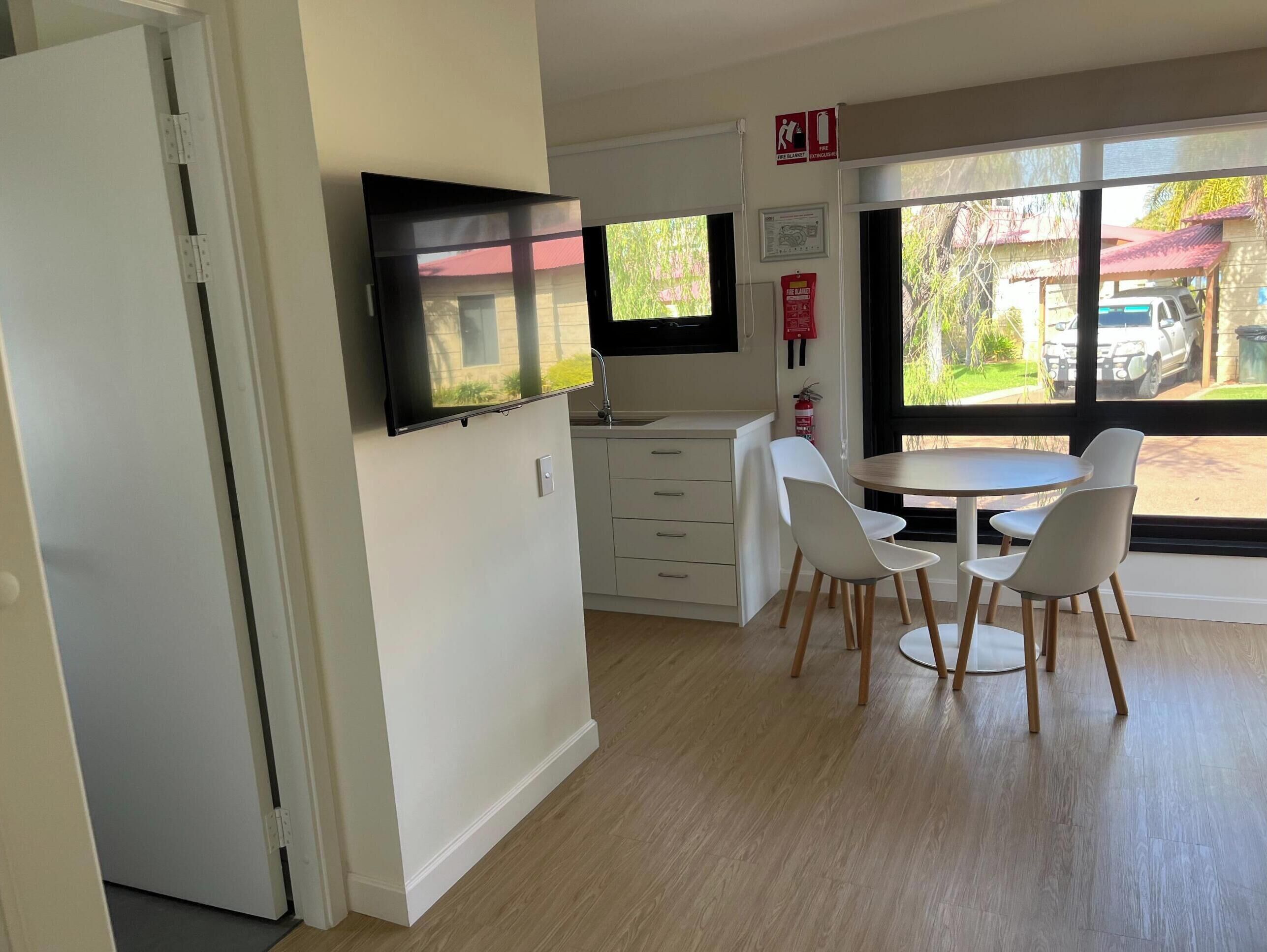 Una cucina moderna con mobili bianchi, una TV a schermo piatto e un'area pranzo con sedie bianche e un tavolo rotondo.