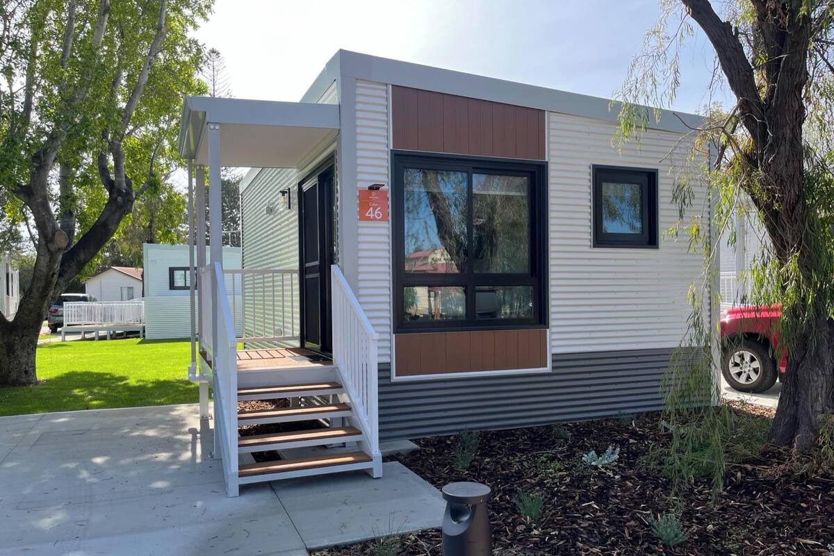 Une maison mobile moderne dotée d’un porche abrité, d’un numéro bien visible, le « 46 », et d’un petit jardin.
