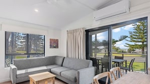 Ein modernes Wohnzimmer mit einem grauen Ecksofa, einem Holztisch und einem Essbereich mit Tisch und Stühlen.