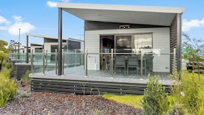 Ein modernes, eingeschossiges Haus mit Terrasse und Glasgeländer, umgeben von Pflanzen.