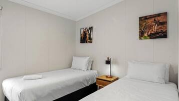 A hotel room with two beds, white bedding, a nightstand with a lamp, and two framed pictures on the wall.