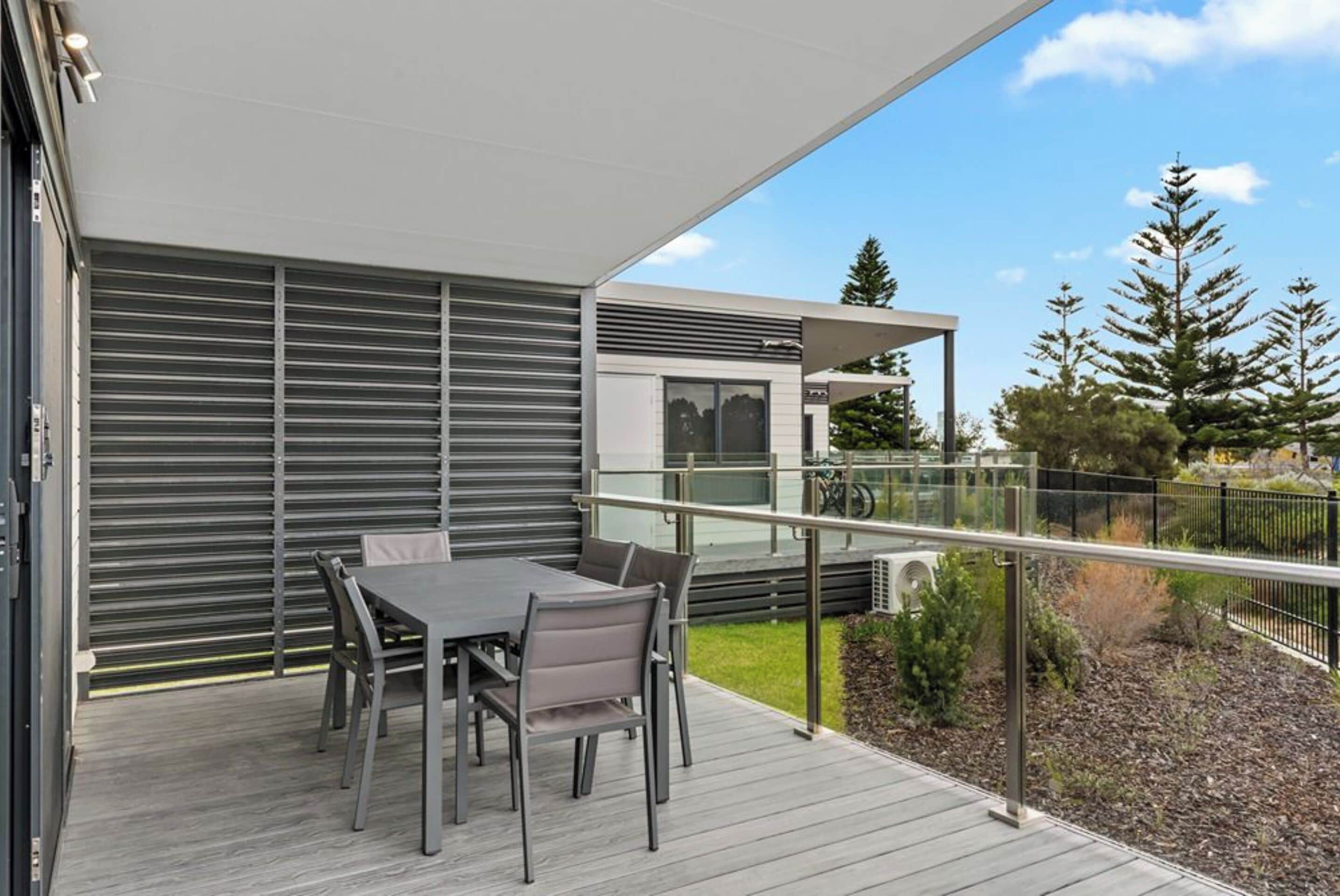 Un patio exterior moderno con una mesa y sillas, un área cubierta y vistas a árboles y un edificio al fondo.