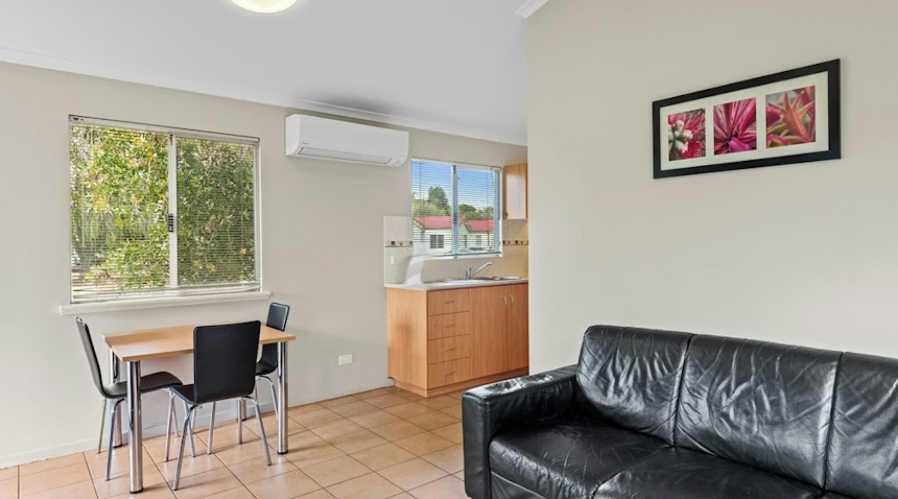A compact living space with a dining area, kitchenette, and a black leather couch.