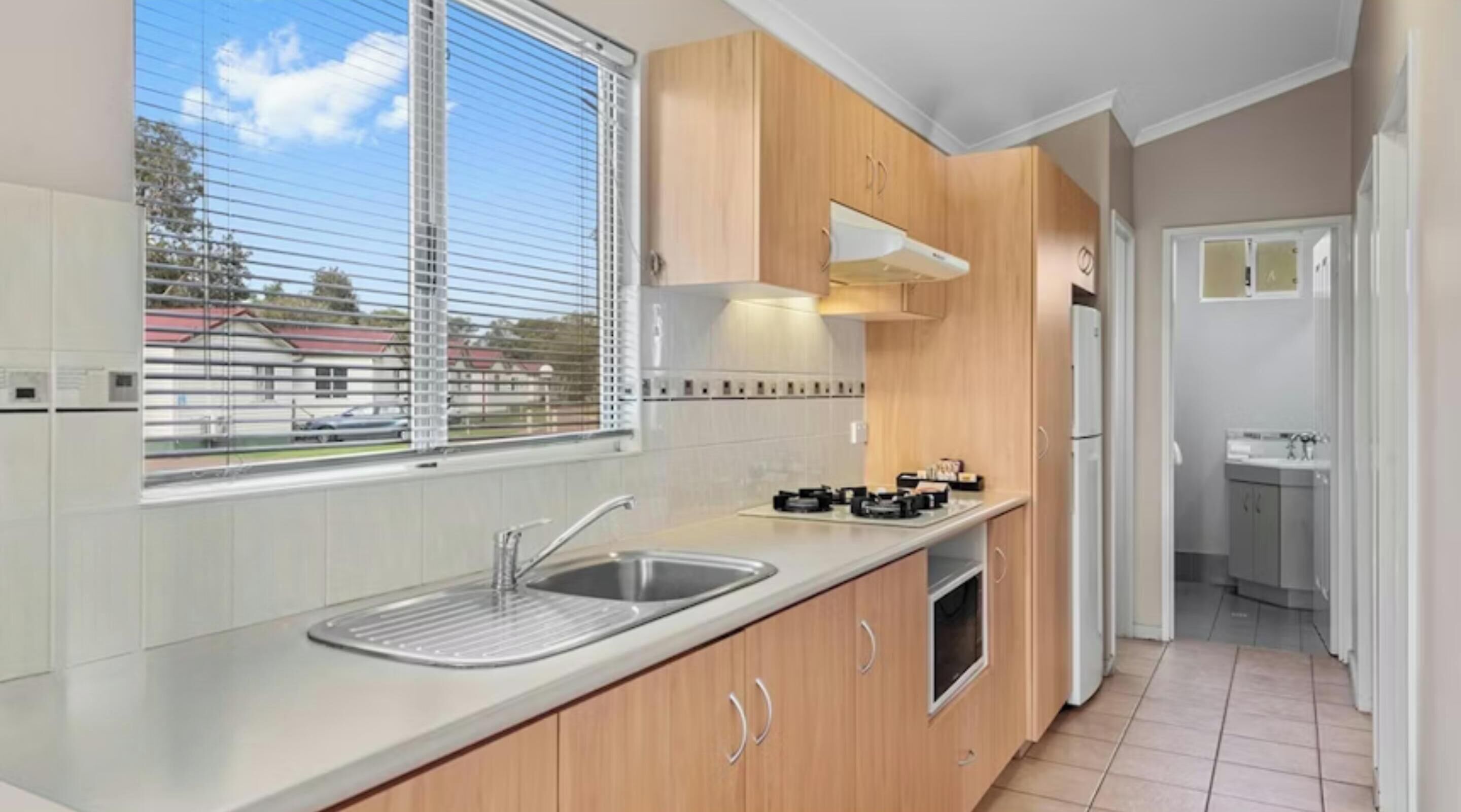 A modern kitchen with wooden cabinets, a stainless steel sink, and a window with blinds.