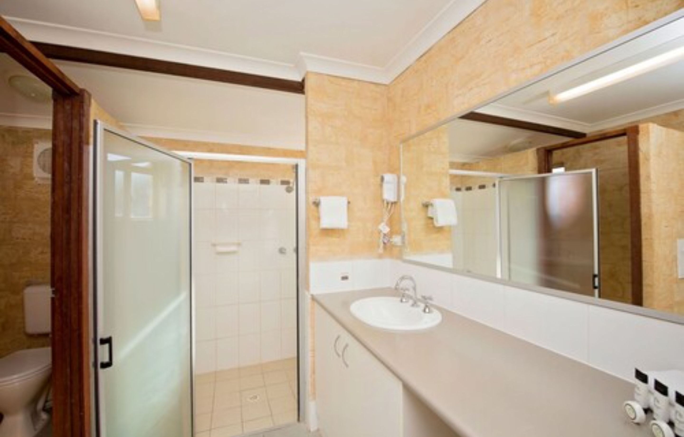 Un baño moderno con cabina de ducha de vidrio, un espejo grande y un lavabo blanco.