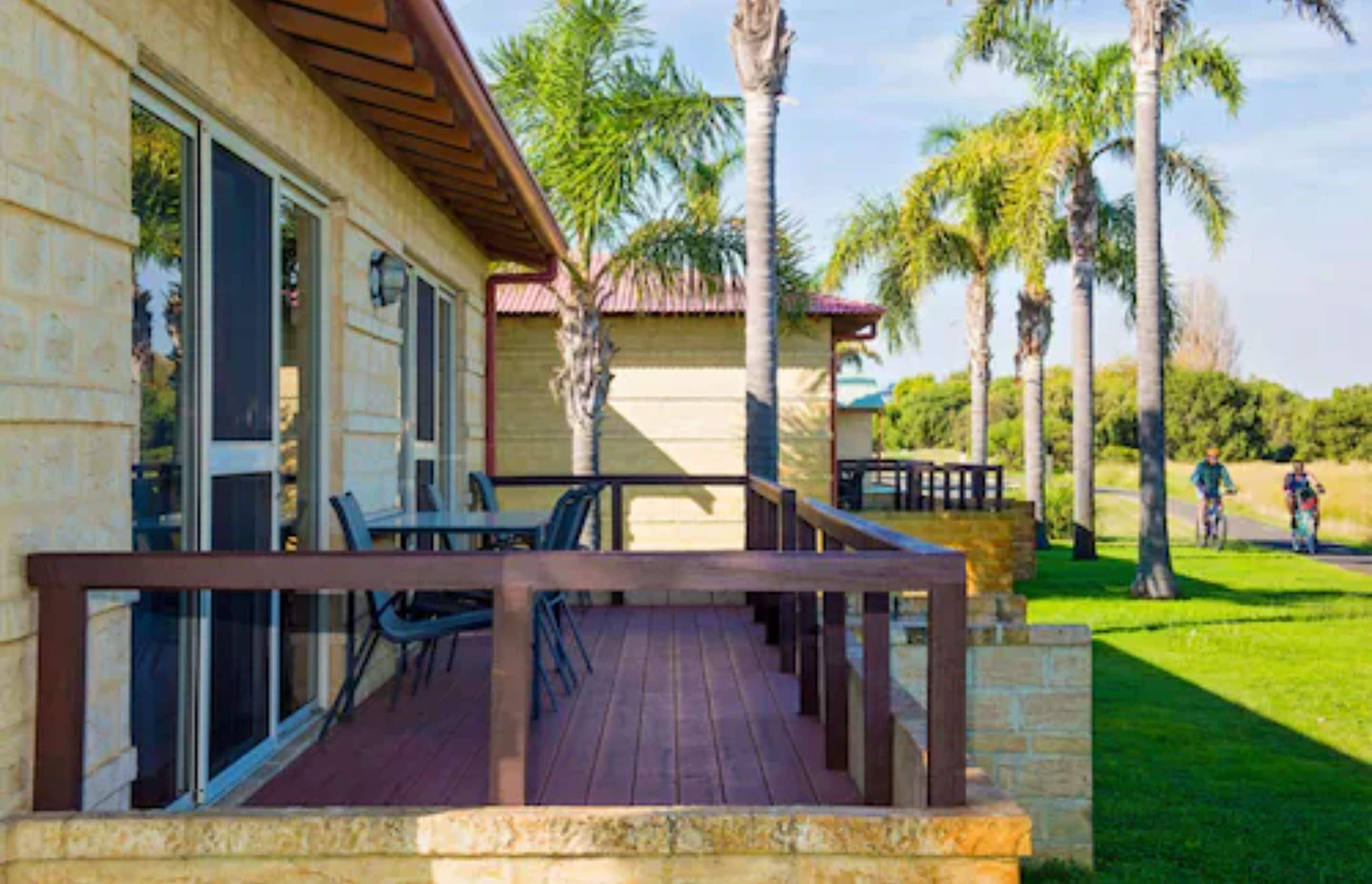 A building with a wooden deck, outdoor seating, and palm trees.