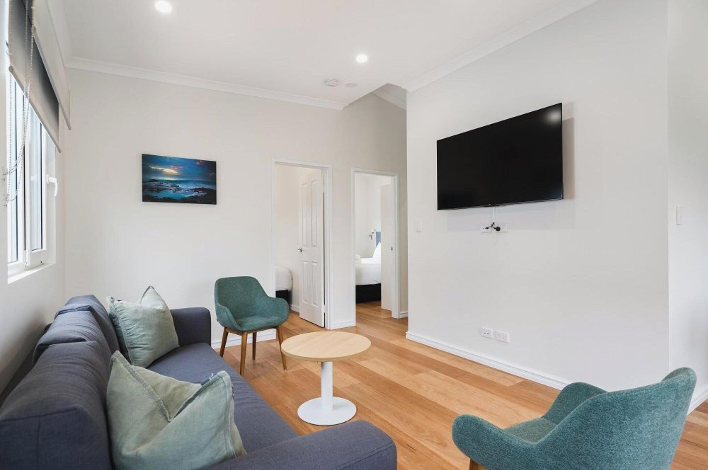 A modern living room with a sofa, chairs, a round table, and a flat-screen TV mounted on the wall.