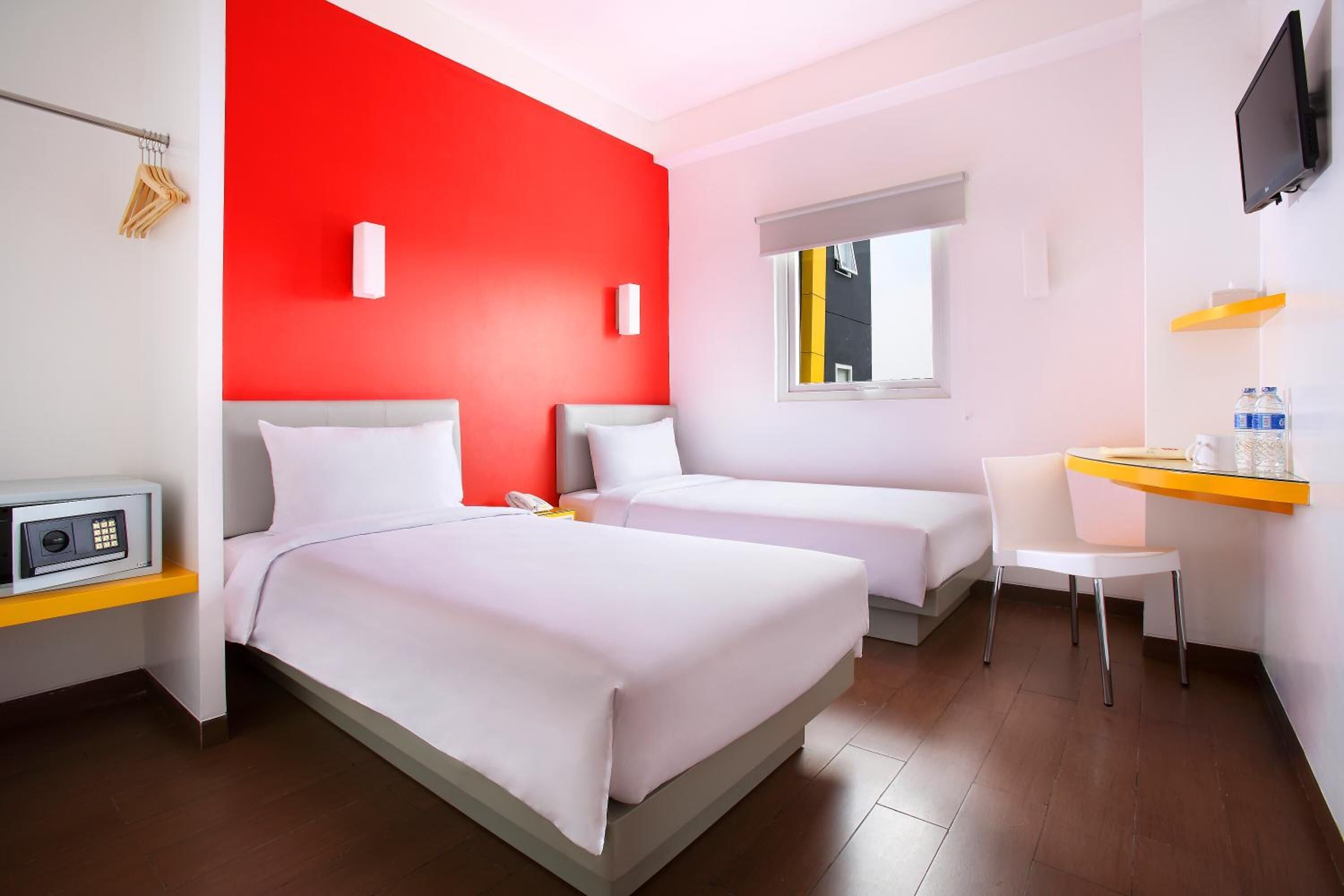 A hotel room with two beds, a desk, a chair, a TV, and a window with a view of a building.