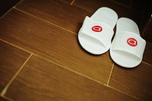 A pair of white slippers with a red logo on a wooden floor. - Amaris Hotel Pakuan Bogor (Bogor)