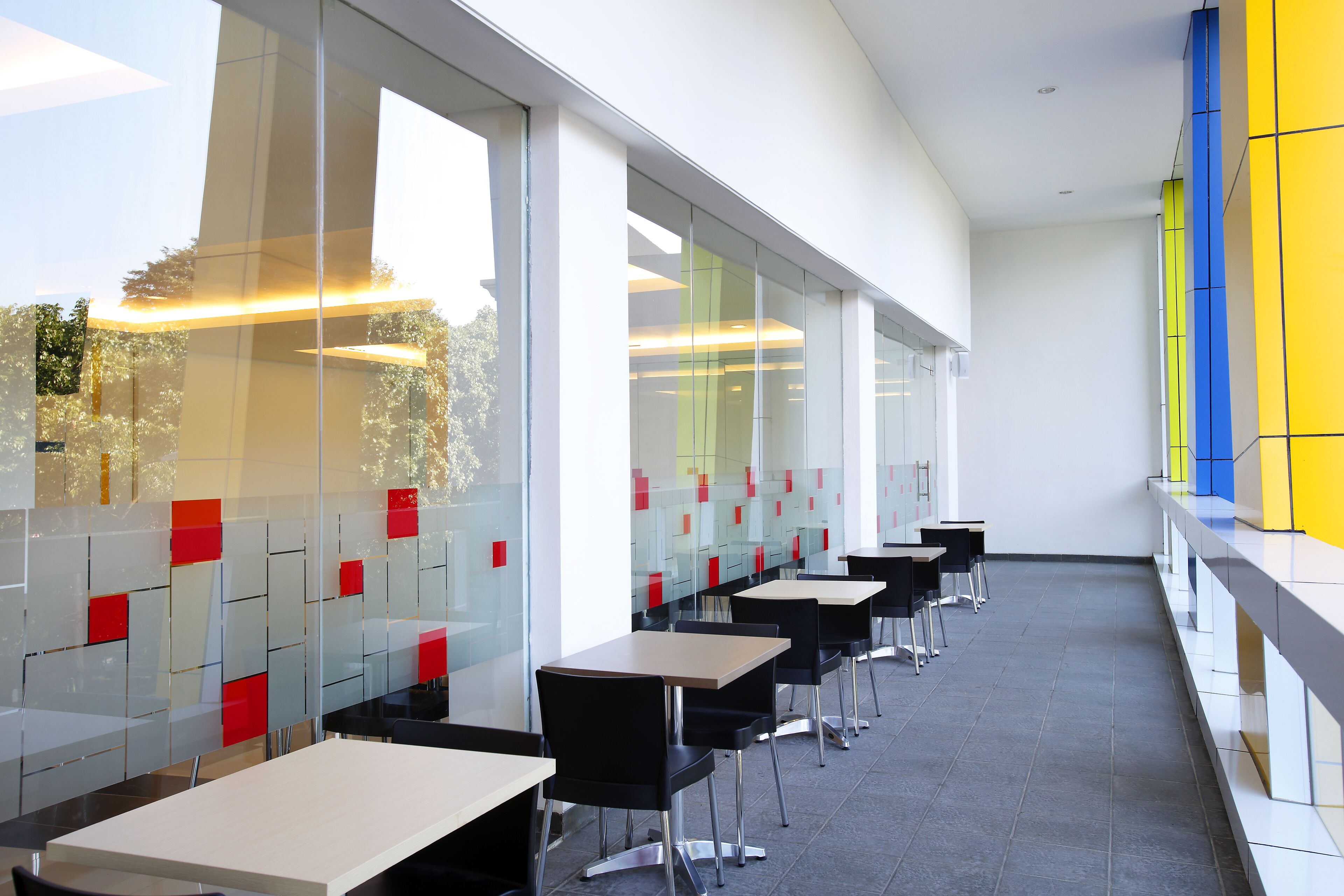 A modern restaurant with glass partitions, black chairs, and white tables.