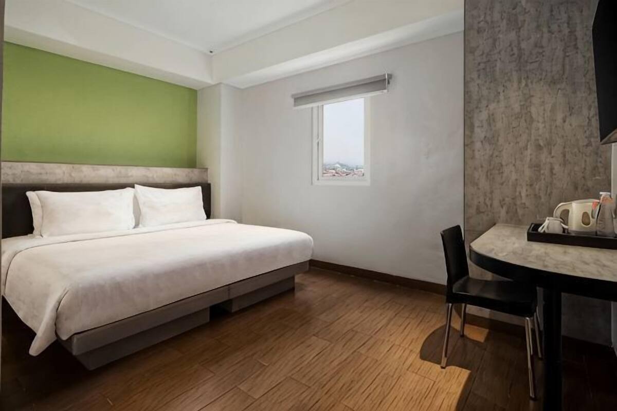A bedroom with a bed, a window, a desk with a chair, and a television.