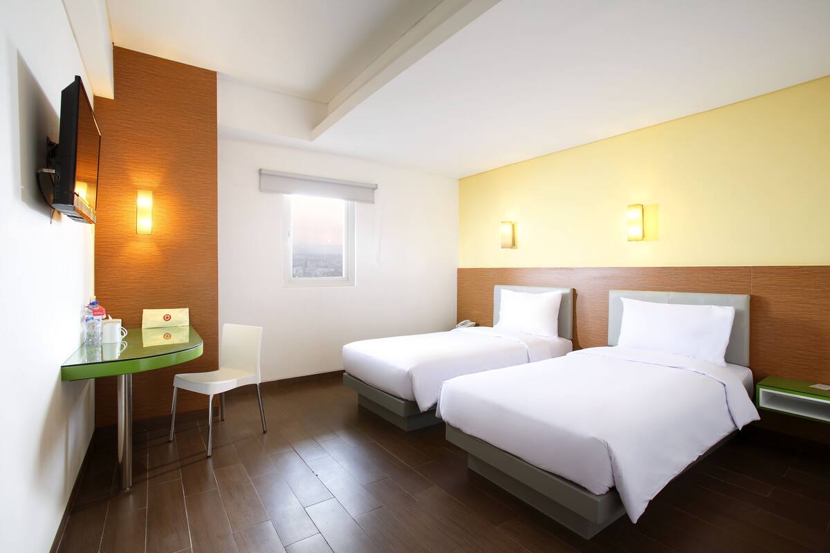 A hotel room with two beds, a desk, a chair, and a TV.