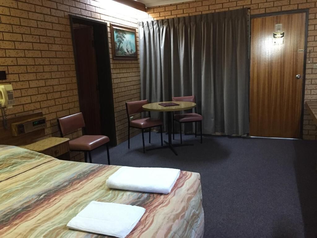 A hotel room with a bed, a small table with chairs, a brick wall, and a door.
