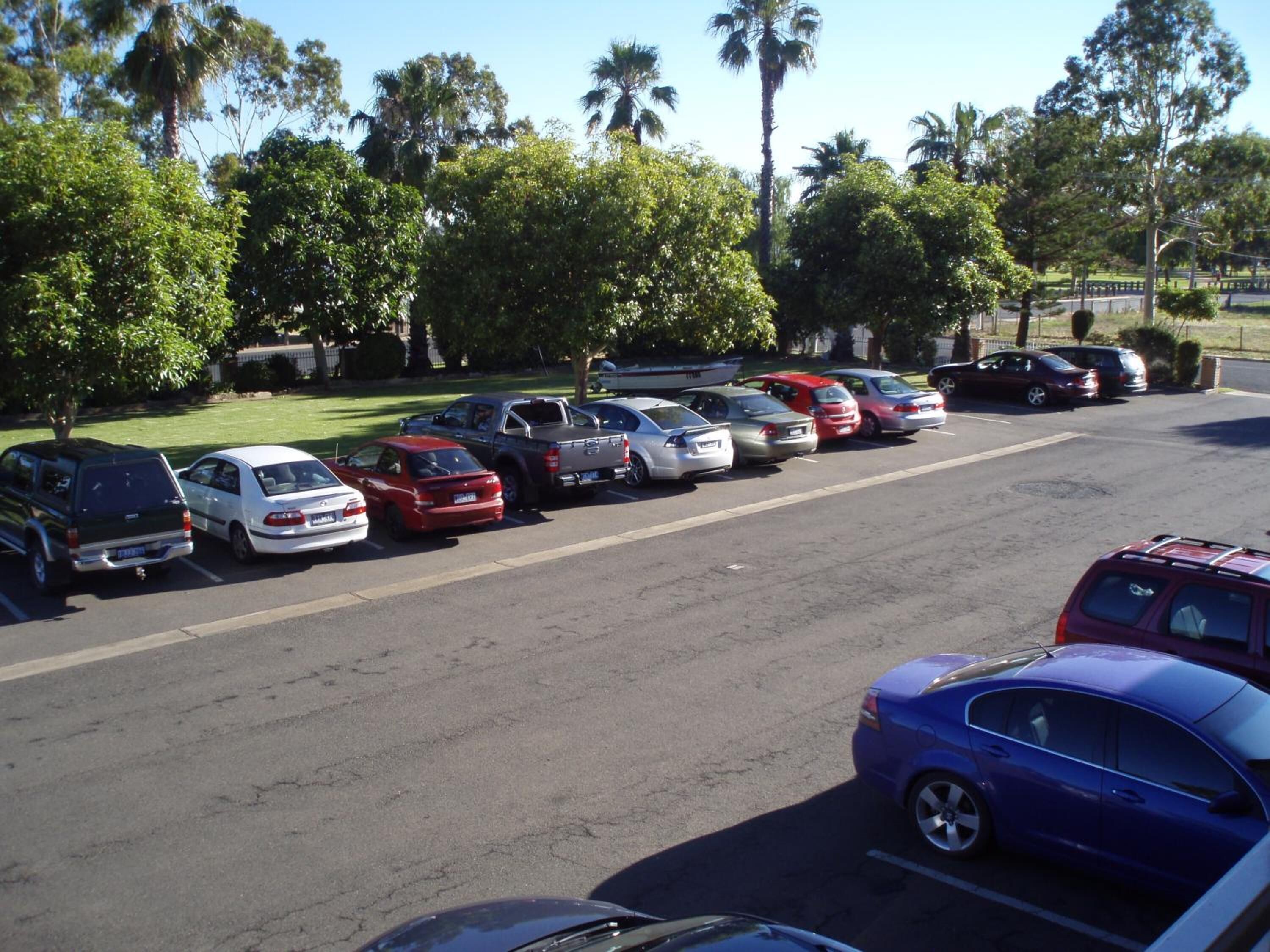 A parking lot with multiple cars parked in rows, surrounded by trees and a clear sky.