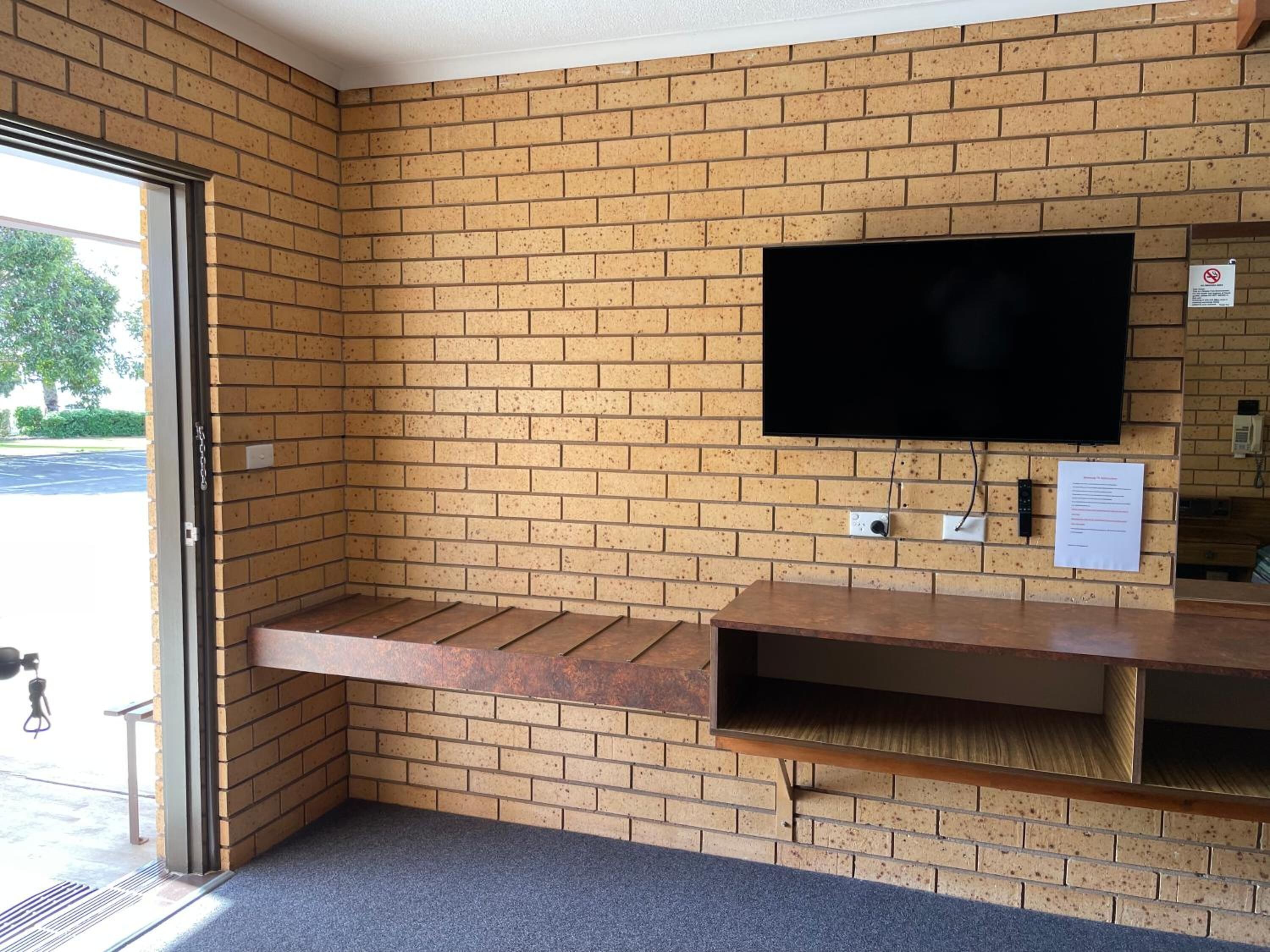Una habitación en esquina con pared de ladrillo, un televisor de pantalla plana montado en la pared y un banco de madera.