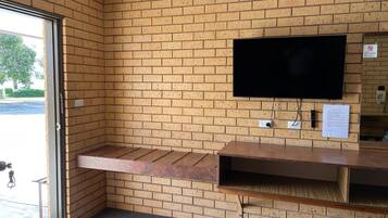 A corner room with a brick wall, a flat-screen TV mounted on the wall, and a wooden bench.