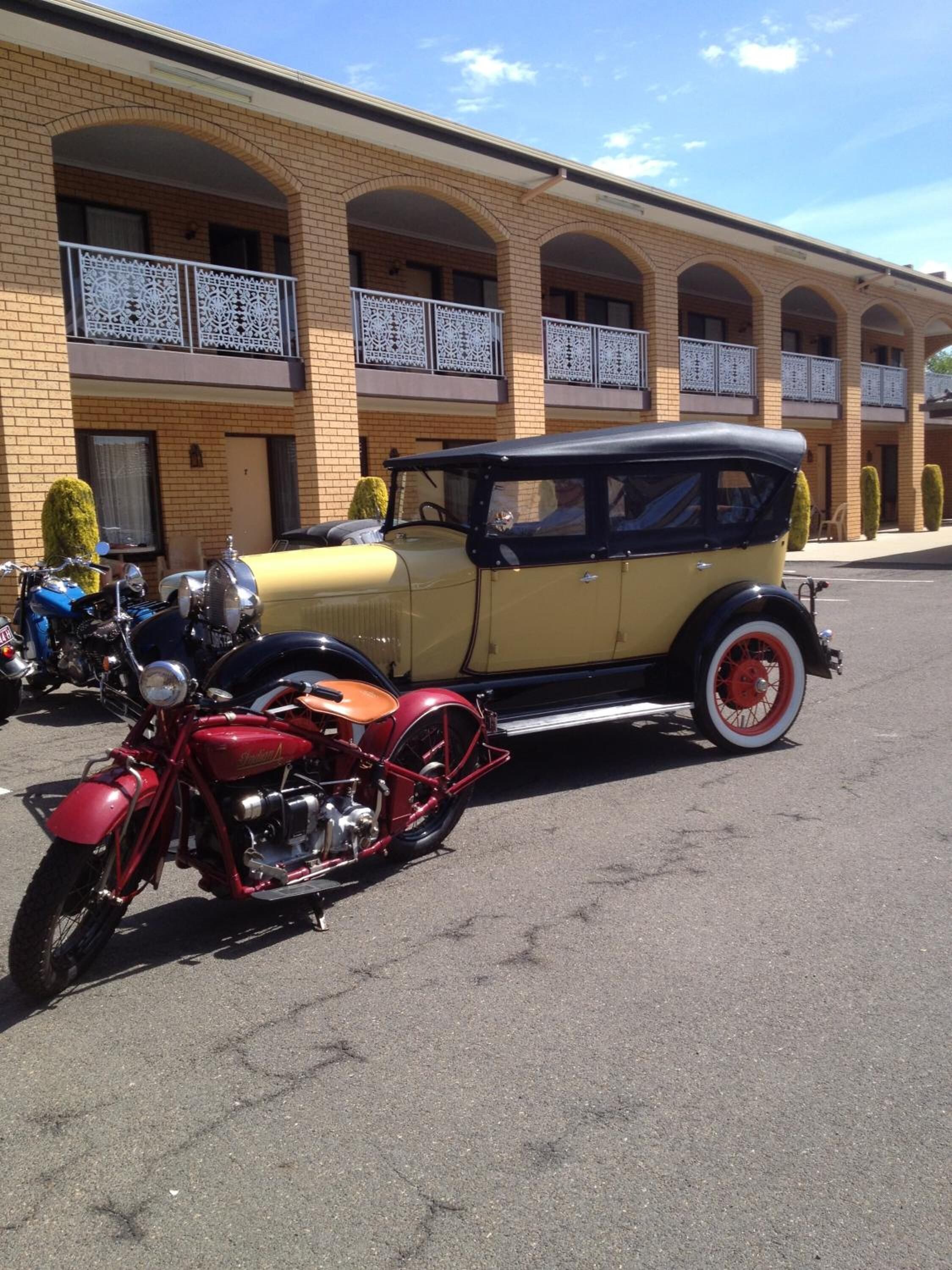 A vintage car and motorcycle parked in front of a building with arched windows and a balcony.