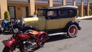 A vintage car and motorcycle parked in front of a building with arched windows and a balcony.