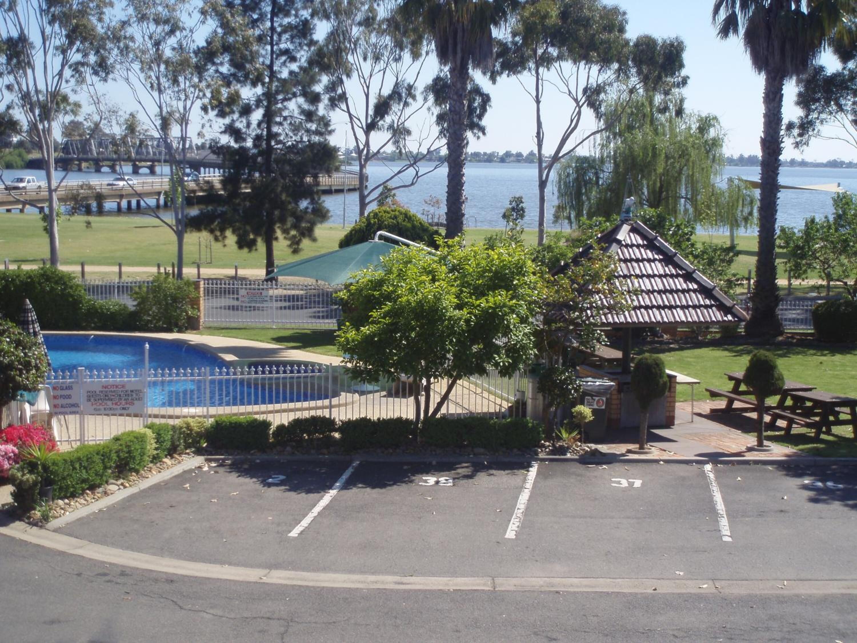 A parking lot with a small gazebo, a pool, and a view of a bridge and water.