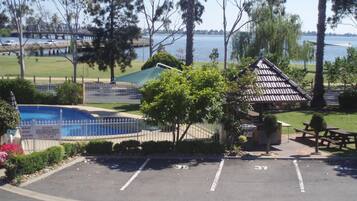 A parking lot with a small gazebo, a pool, and a view of a bridge and water.
