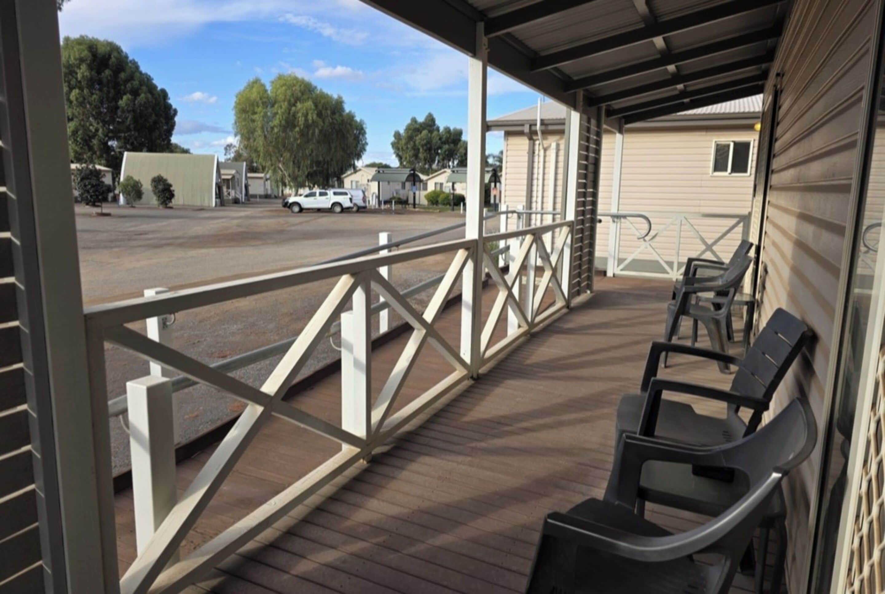 A covered outdoor area with a wooden deck, metal railing, and a few plastic chairs.
